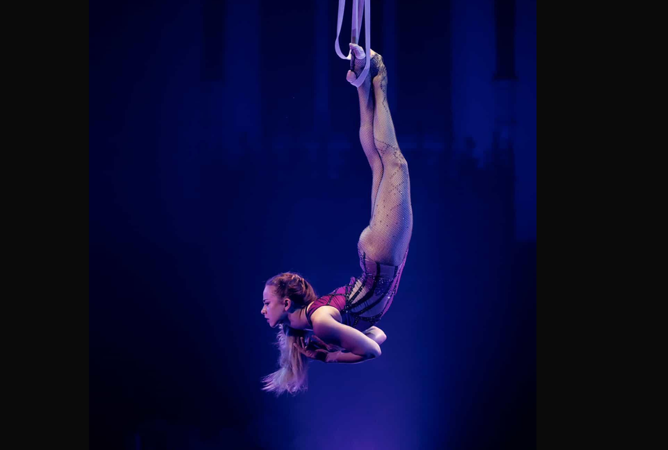 Female aerialist performing single heel hang on aerial straps - grip provided by AcroGrip liquid chalk