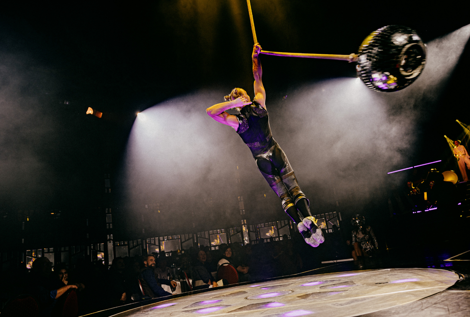 Rope circus artist performing disco ball act on stage. Single arm hand grip on rope