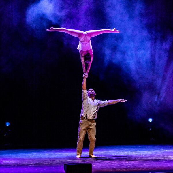 Two acrobats performing on stage with a dark background and purple lighting.